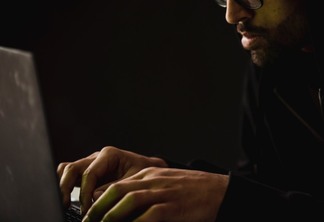 crop bearded man working on laptop in darkness