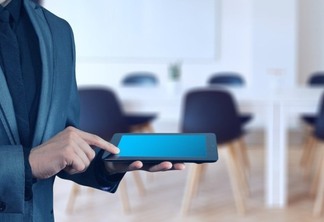 Homem de terno com tablet na mão e sala de reunião de fundo